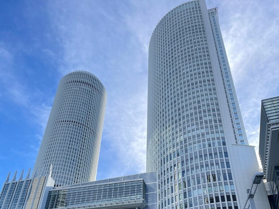 Two tall modern skyscrapers against a blue sky in Nagoya, Japan.