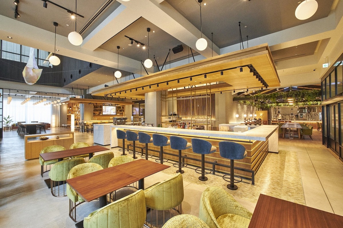 Interior photo of Nikko Style Nagoya hotel's restaurant. The modern restaurant interior featuring wooden beams and stylish seating, with a central bar area and large windows allowing natural light.