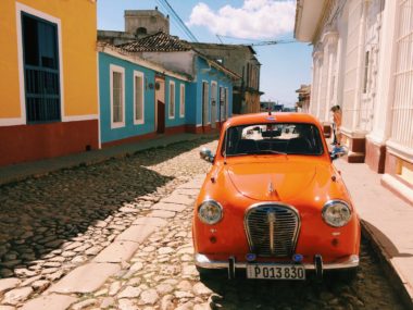 Orange classic car parked on cobblestone road in Trinidad, Cuba