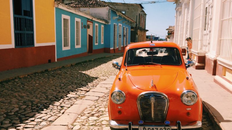 Orange classic car parked on cobblestone road in Trinidad, Cuba