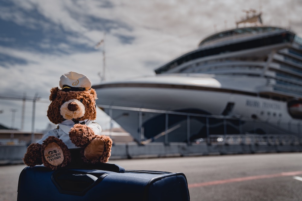 Princess Cruises teddy bear on top of luggage with cruise ship in the background