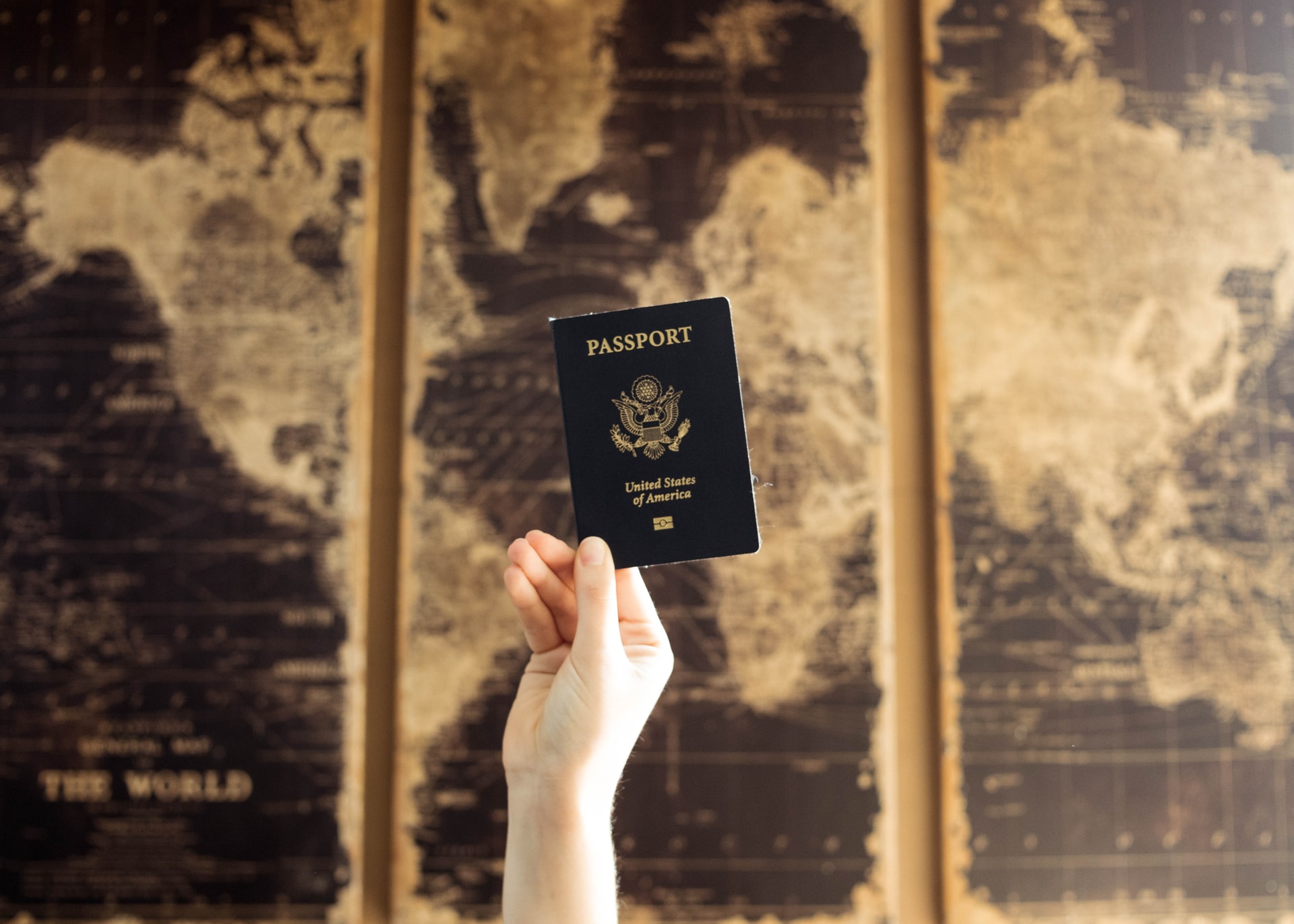 hand holding american passport in front of world map