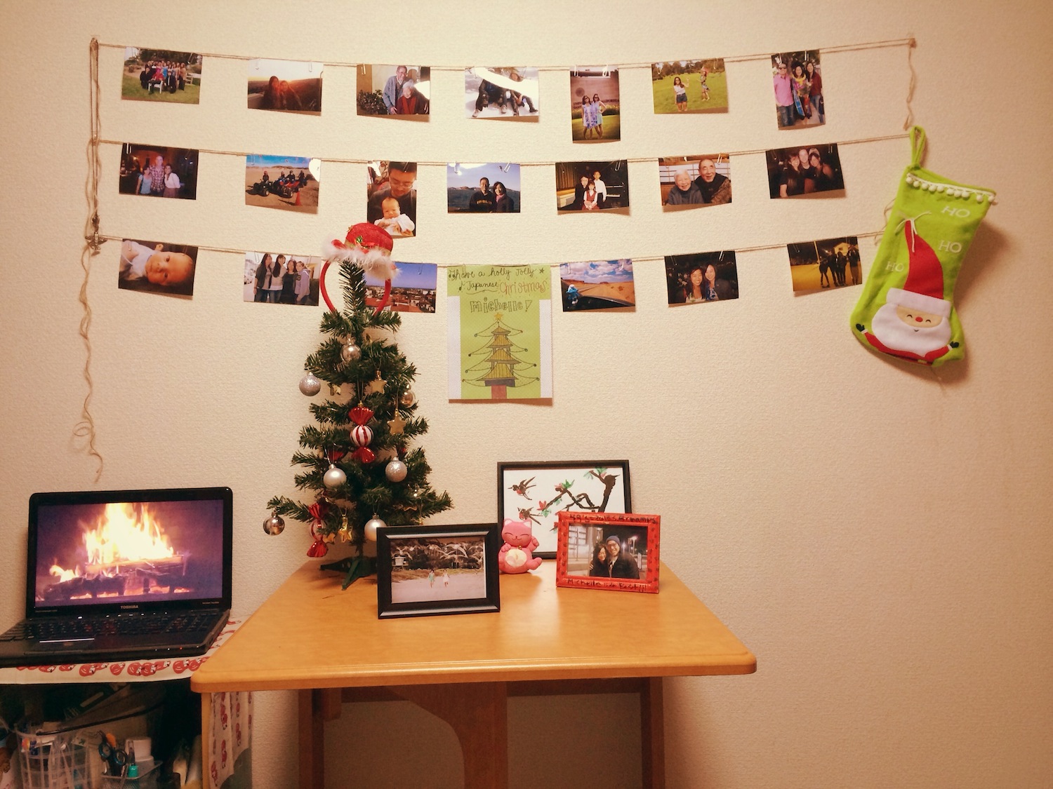 photo wall with pictures on strings, picture frames, lit fireplace on a laptop, and mini Christmas tree
