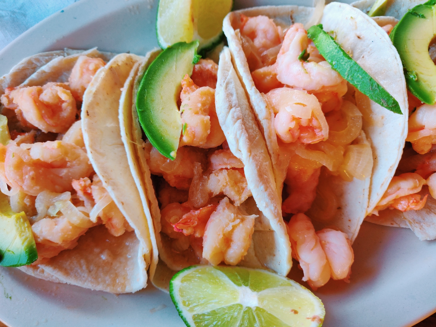 Shrimp tacos cooked in a butter and garlic sauce, topped with grilled onions and avocado and served with lime wedges