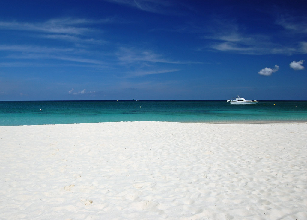 Seven Mile Beach in Grand Cayman: wide and secluded stretch of white sand in foreground with green and blue waters and navy skies with a small boat in the background