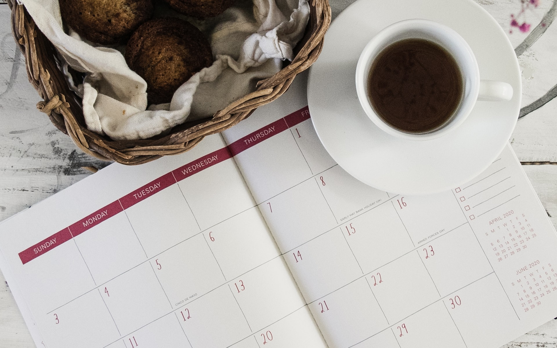 planner opened to monthly calendar with red accents; coffee cup on saucer
