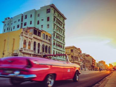 pink convertible driving into sunset past colorful buildings in Havana Cuba