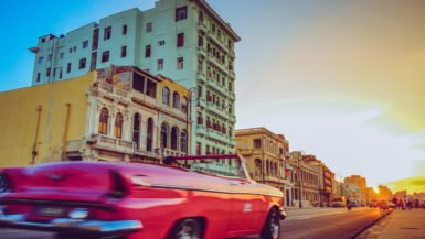 pink convertible driving into sunset past colorful buildings in Havana Cuba
