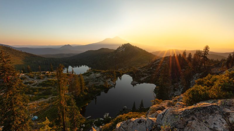 sunset view on top of mountain looking down on tall trees, mountains, and lakes in valleys