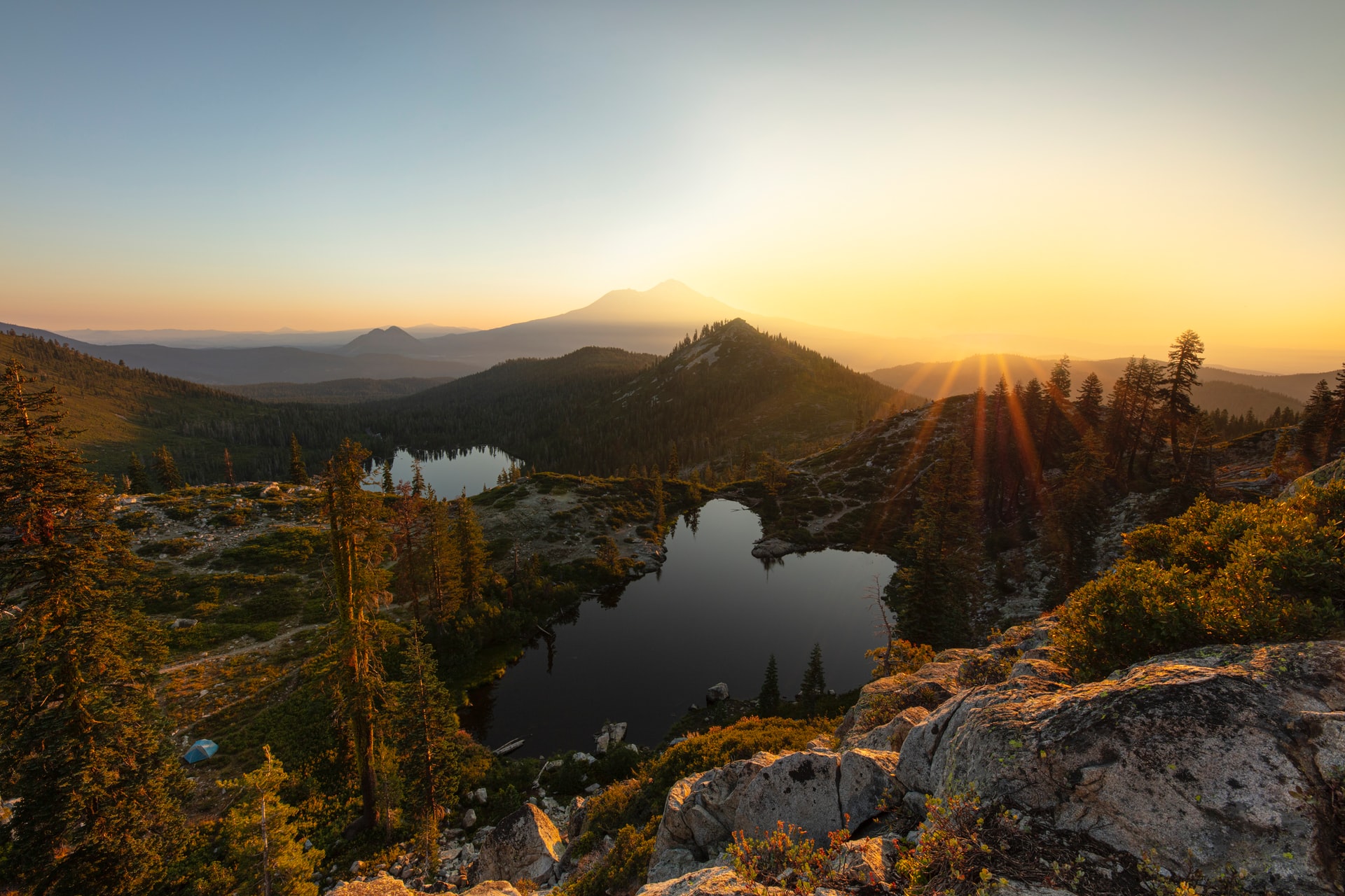 sunset view on top of mountain looking down on tall trees, mountains, and lakes in valleys