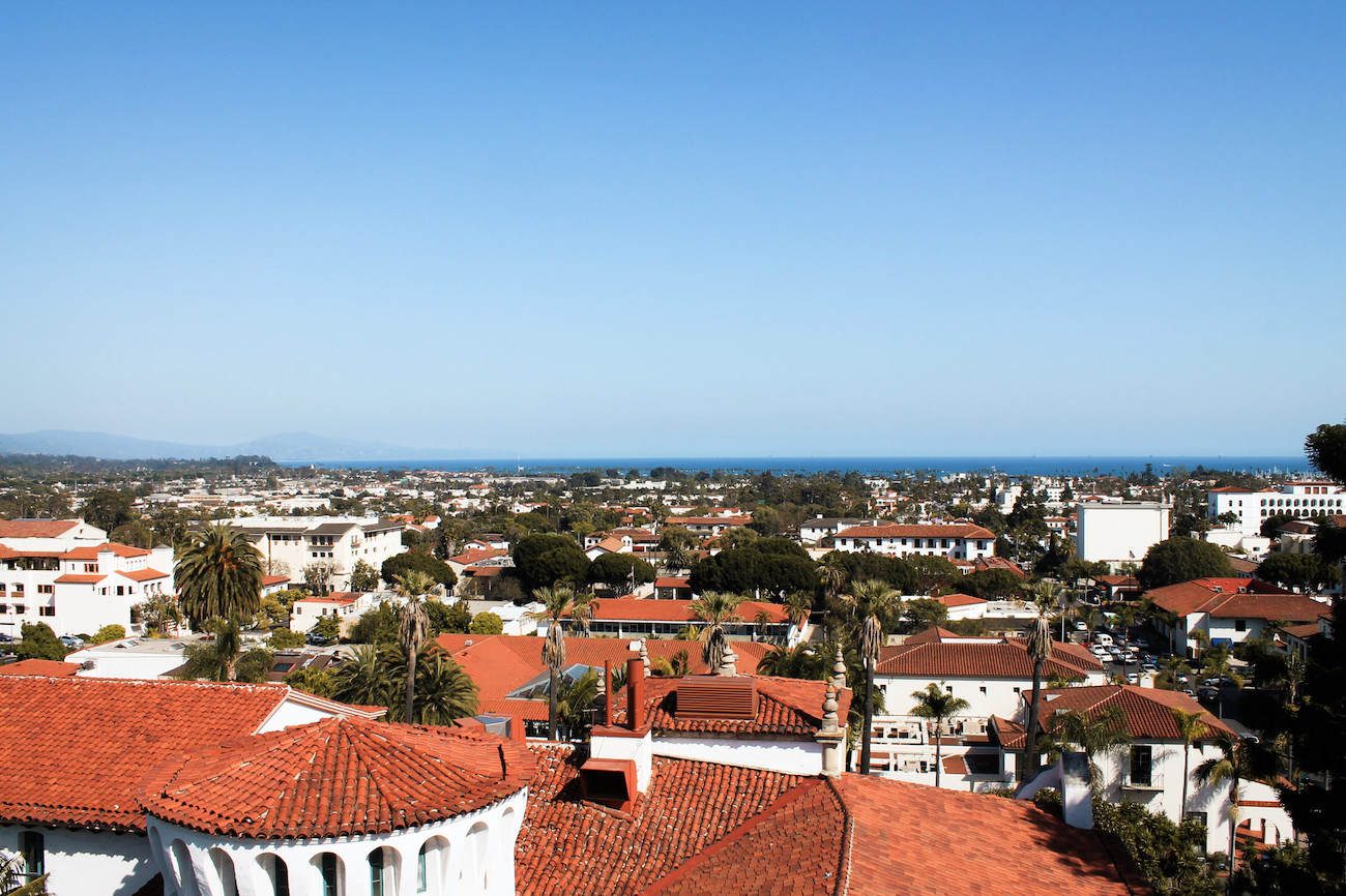 Rooftop view of downtown Santa Barbara: red tiled roofs on top of white painted buildings, ocean in the distance