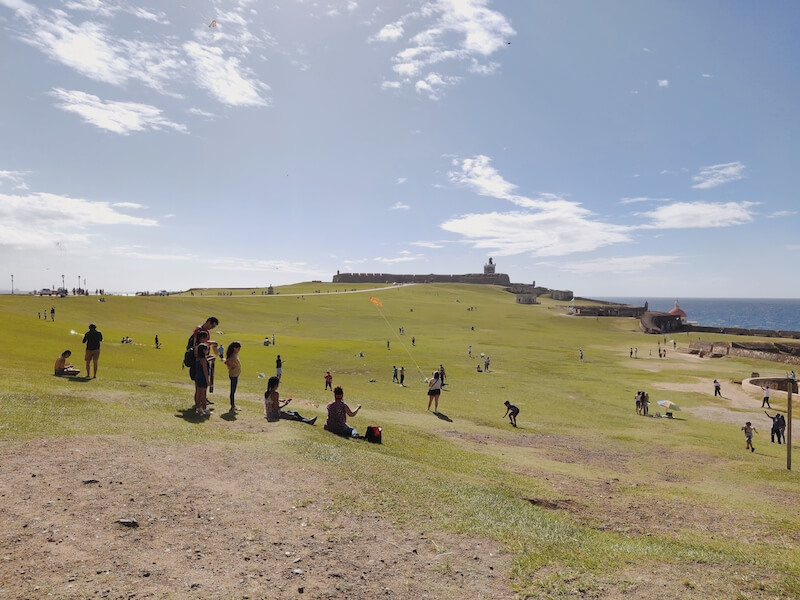 Lawn outside El Morro Fortification with adults and children lounging on the grass and flying kites