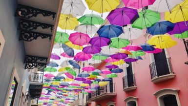 Famous Instagram street in Old San Juan known as Umbrella Street or Calle de Fortaleza; colorful umbrellas hang over the street outside brightly painted buildings
