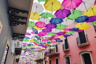 Famous Instagram street in Old San Juan known as Umbrella Street or Calle de Fortaleza; colorful umbrellas hang over the street outside brightly painted buildings