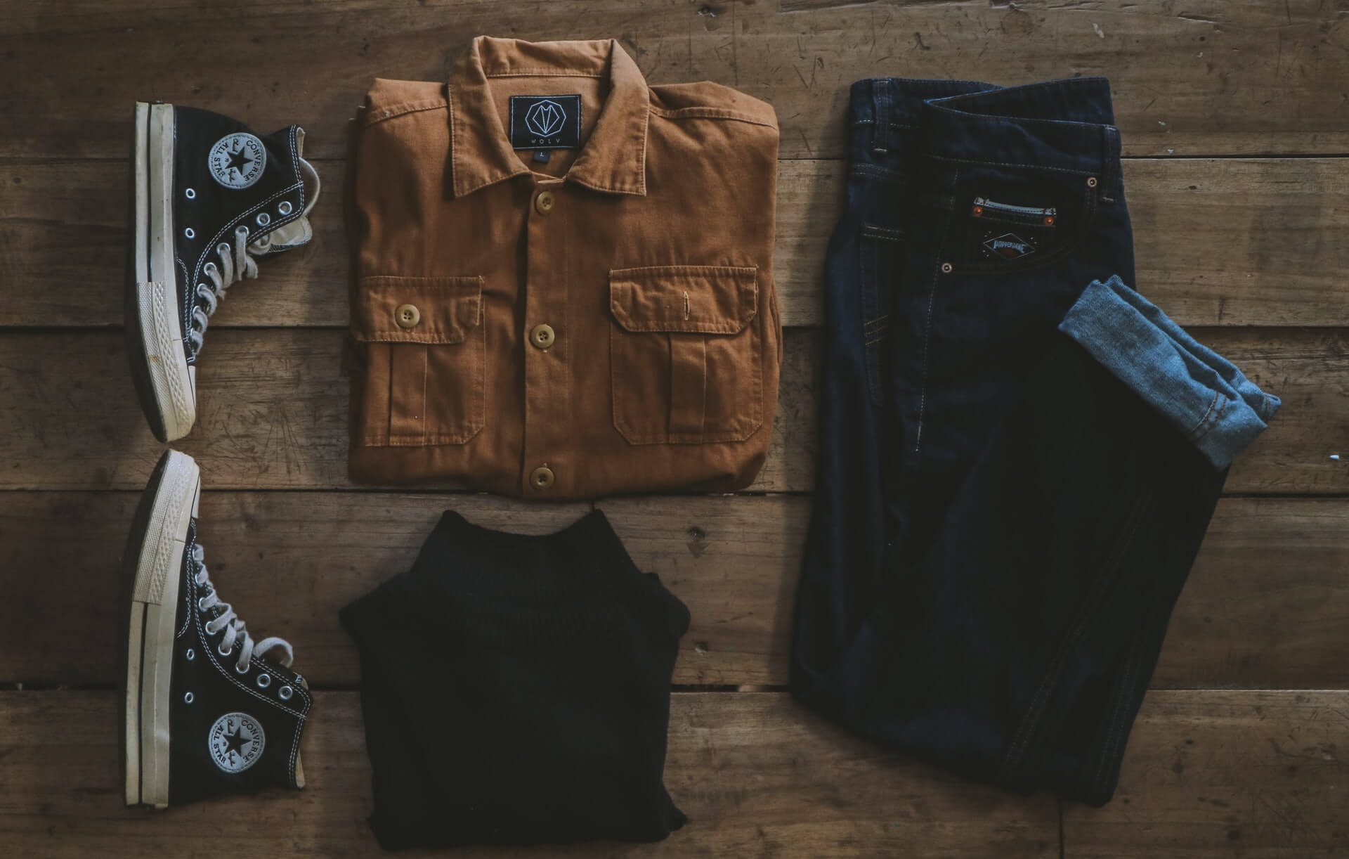 flatlay of tan button-down shirt, black converse sneakers, and dark blue denim jeans