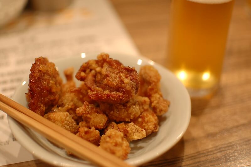 popular japanese food and izakaya snack, chicken karaage. Served in a white dish next to a beer and chopsticks