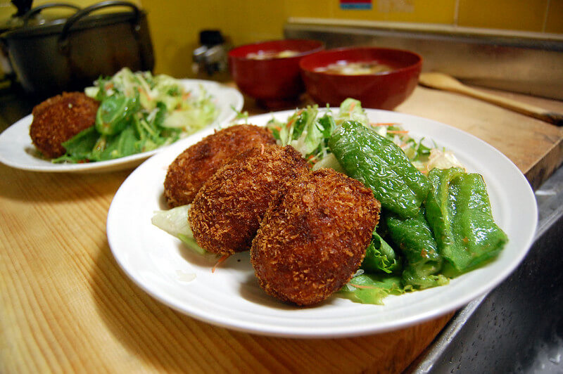 japanese side dish korokke served on a white plate alongside green vegetables