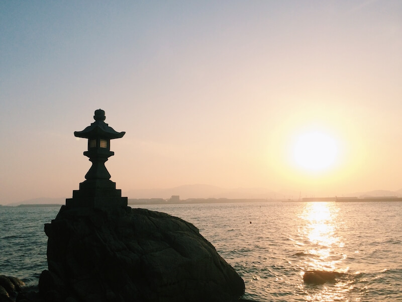 silhouette of a japanese stone lantern at sunset and the ocean in the background