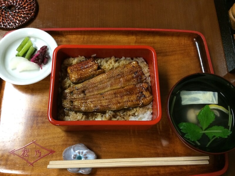 popular japanese food unagi presented over rice on a tray with pickled condiments, soup, and chopsticks