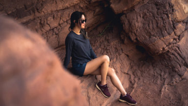 Girl sitting on red rocks wearing KUHL's Konstance Sun Protection Long Sleeve in black/charcoal and women's Freeflex Hiking Short in Rainstorm blue