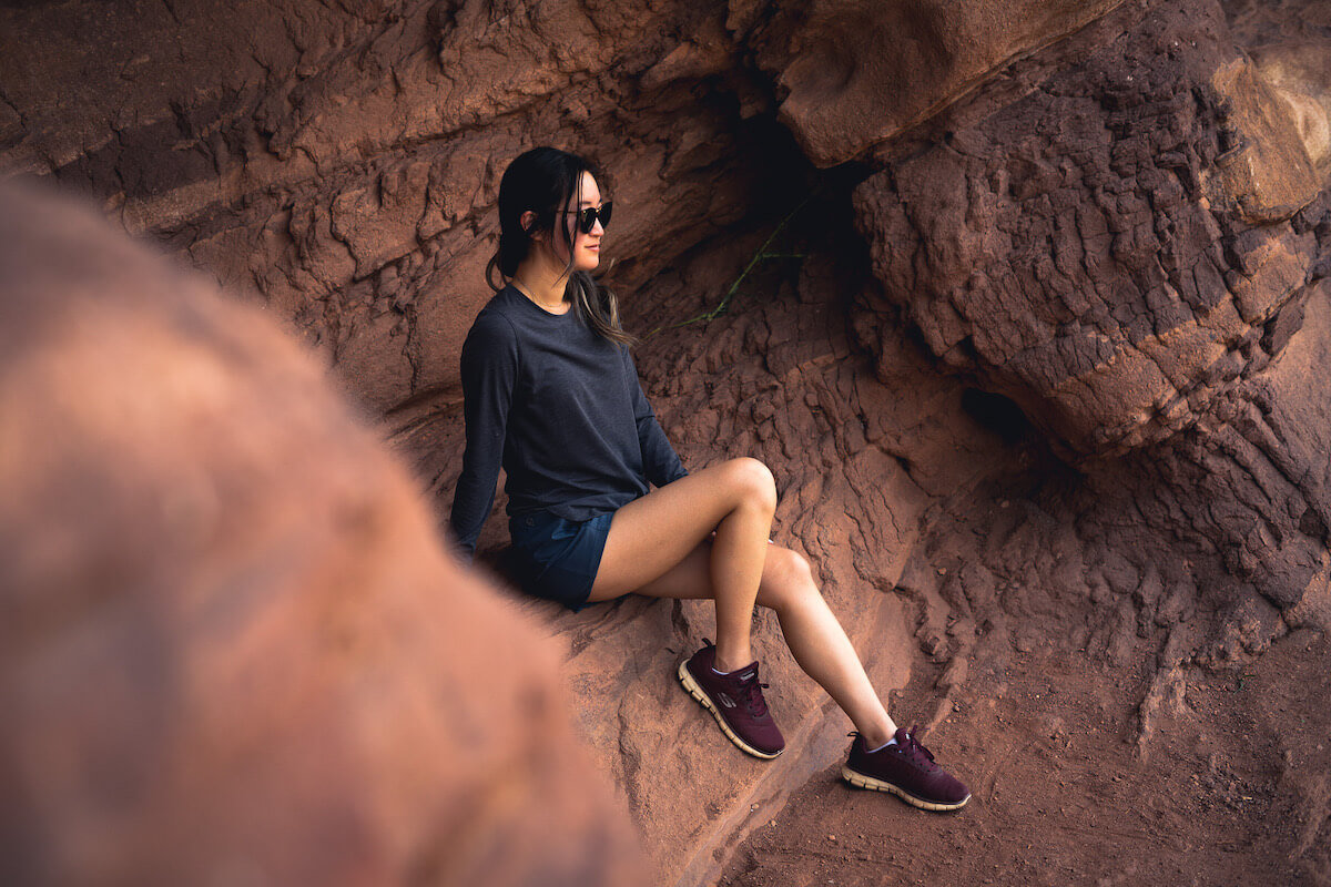 Girl sitting on red rocks wearing KUHL's Konstance Sun Protection Long Sleeve in black/charcoal and women's Freeflex Hiking Short in Rainstorm blue