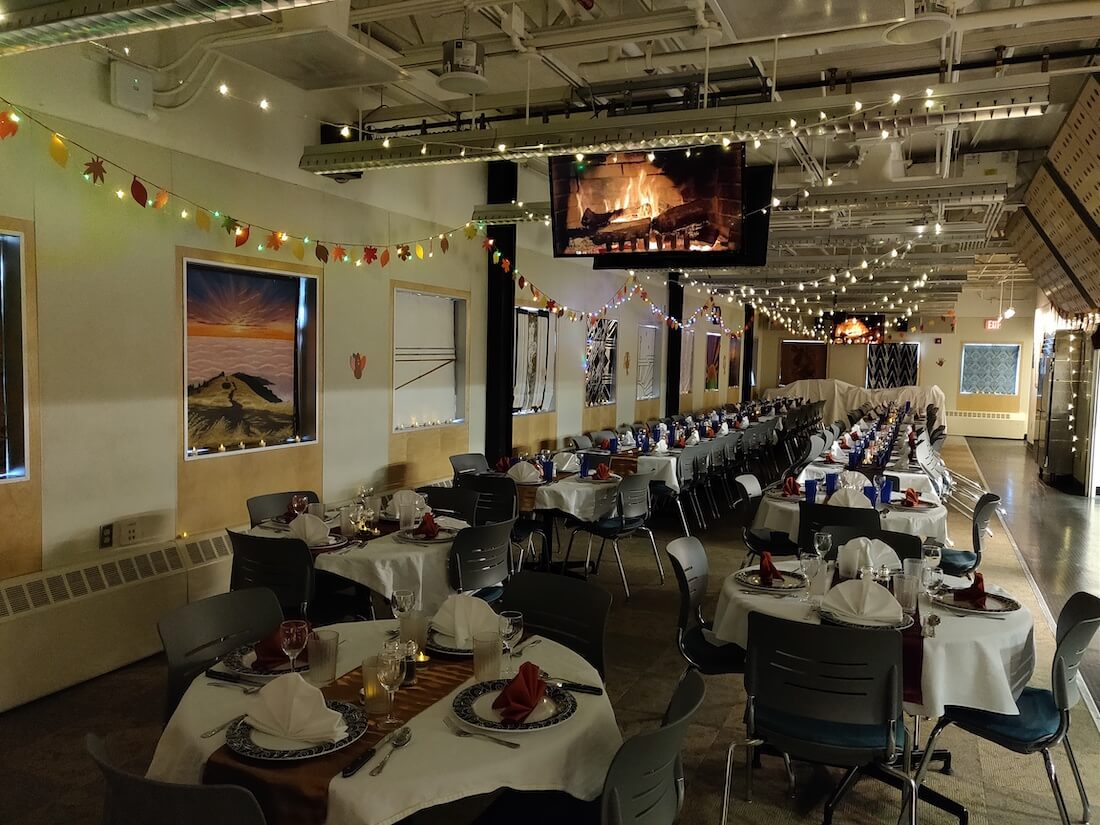 The South Pole's dining room decorated and set for a holiday meal. The TVs show a digital fireplace, tables are formally decorated, and fairy lights are strewn across the ceiling