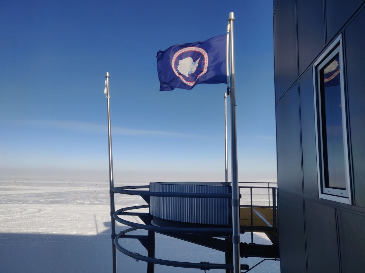 The South Pole Station's Observation Deck. Includes a USAP flag, observation deck, flat ice, and the side of a building