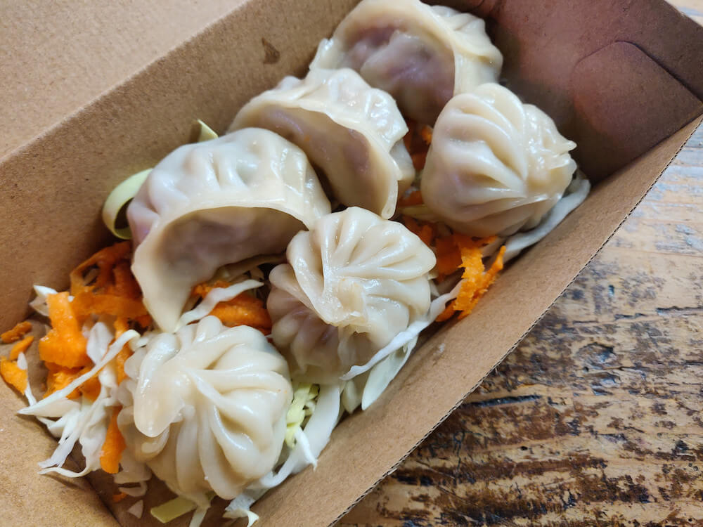 Six steamed Nepalese steam dumplings on a bed of sliced carrots and cabbage in a takeaway box