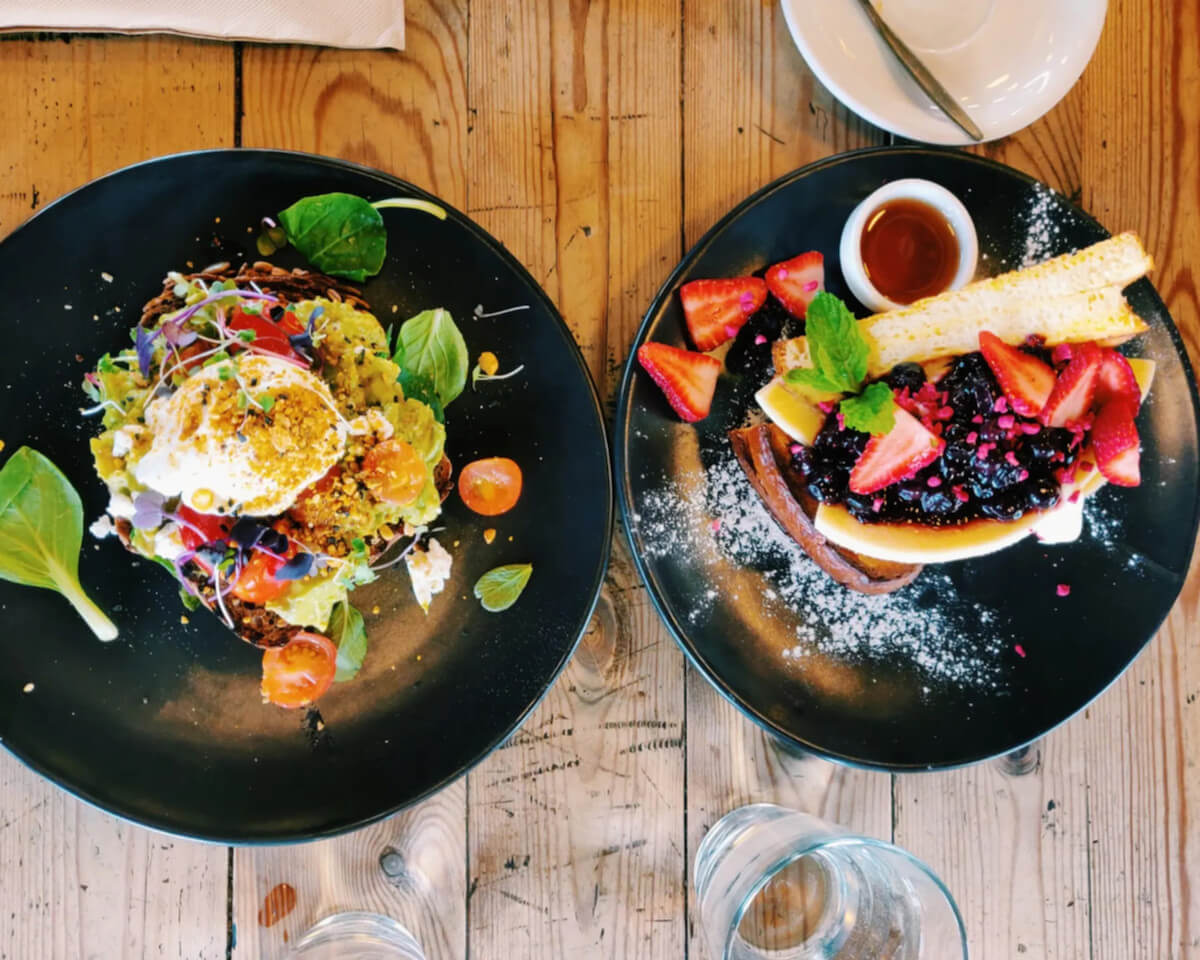 Two brunch items from top Christchurch restaurant Unknown Chapter Coffee Roasters: Avocado Toast with halloumi, tomatoes, sprouts, and poached egg; French Toast with berry compote and fresh strawberries