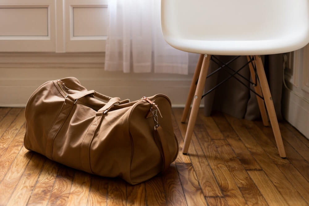 brown duffel bag sits on a hardwood floor