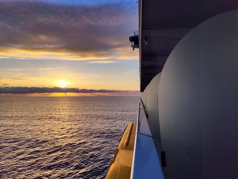 sunset at sea from a stateroom balcony with lifeboats hanging under deck