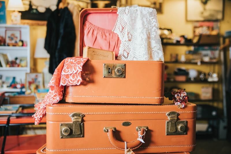 two orange vintage suitcases stacked on top of each other. The top one is opened and displays a book and lace.