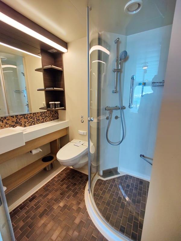 cruise ship bathroom includes a toilet, shower with glass shower door, shelving, and amenities