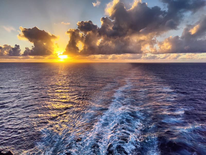 Sunset at sea with waves from ship as it sails away