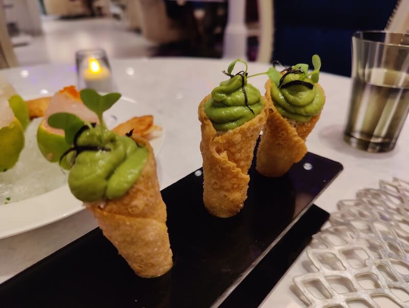 three fried cones with green mousse swirling out sit in a customized dark-wood holder