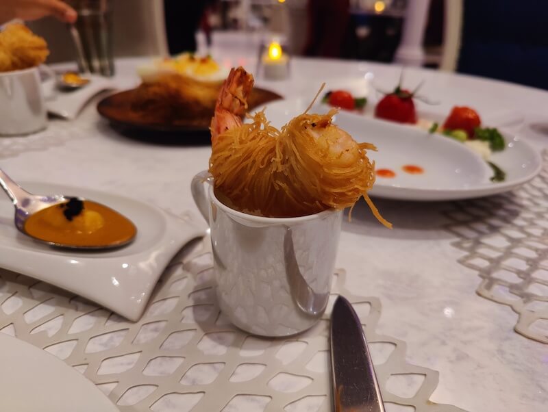 a crispy fried jumbo shrimp sits in a small serving mug