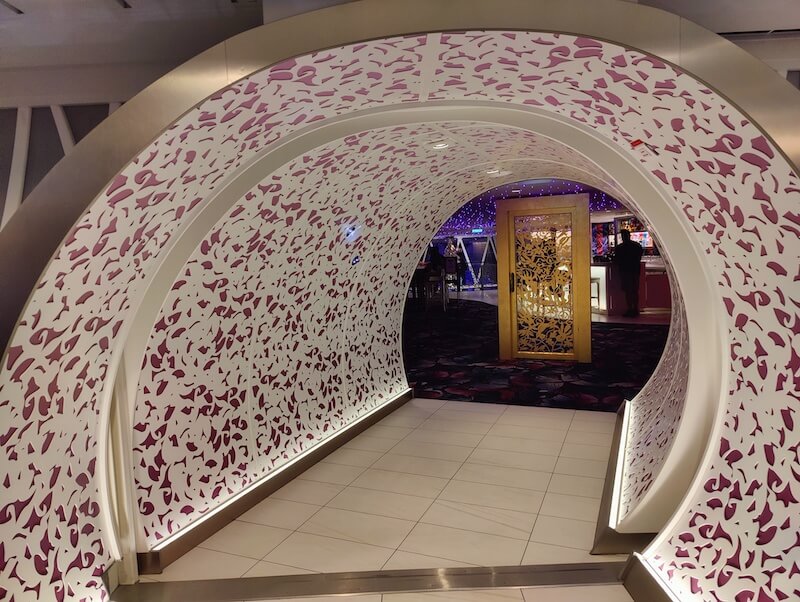 a whimsical pink and white tunnel leads to a standalone golden door inside Royal Caribbean's Wonderland restaurant