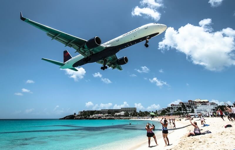 An airplane flies over Maho Beach in St. Maarten as beachgoers take photos of the low landing