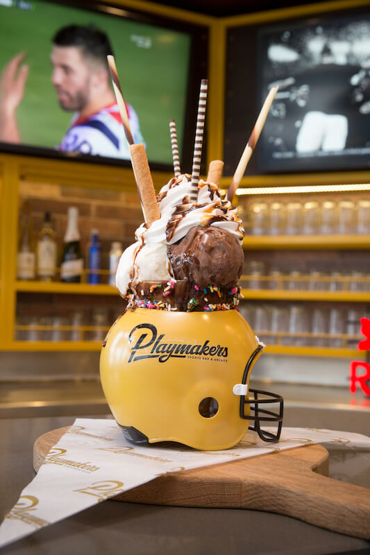 Royal Caribbean's Playmakers Sports Bar & Arcade featuring an ice cream sundae served in a football helmet with sports games playing on big-screen TVs behind