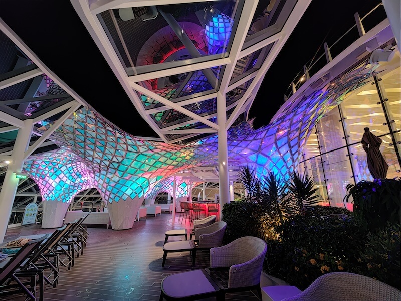 The solarium in Symphony of the Seas. Includes lounge chairs and structural decoration with a net pattern that includes ambiance lighting at night