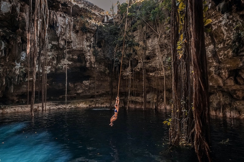 A woman swings froma vine over a pool of freshwater in a cenote in Mexico