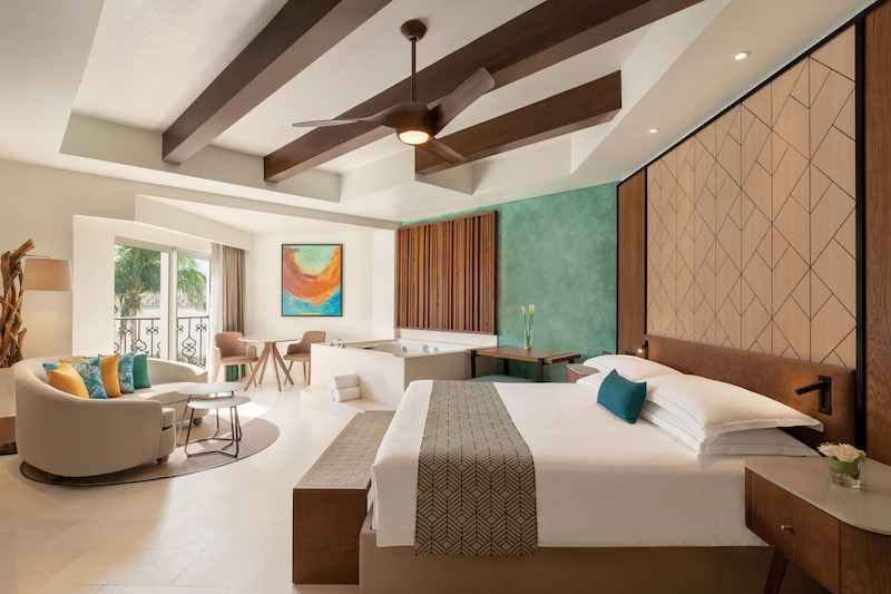 A suite in the Hilton Playa del Carmen Adults-Only All-Inclusive Resorts. Photo includes a king size bed, seating area, small dining table, and large soaking tub