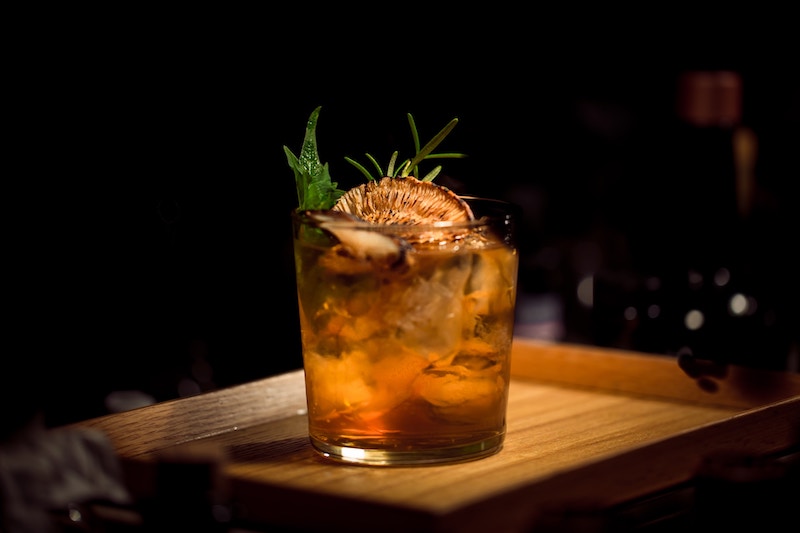 A short glass is filled with a dark orange cocktail and garnished with dried fruit and herbs