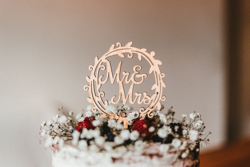 A white wedding cake with rustic floral decorations topped with a circular "Mr & Mrs" cake topper