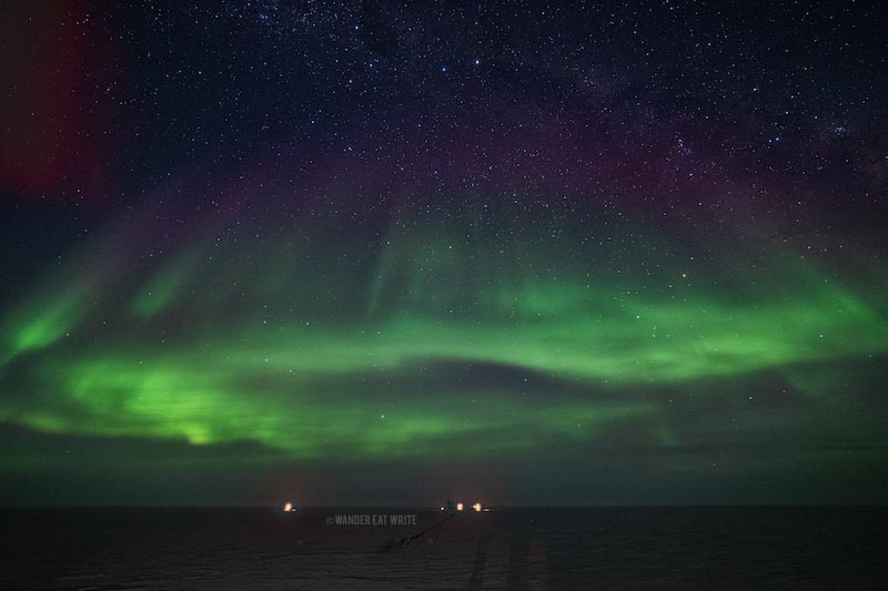 Neon green Aurora Australis in Antarctica over building lit in red lights at the South Pole
