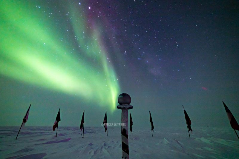 Green aurora australis and the ceremonial south pole and its flags with the night sky