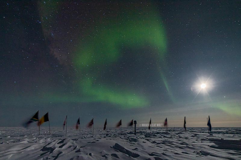 Light green aurora australis and the bright moon over the ceremonial south pole and its flags