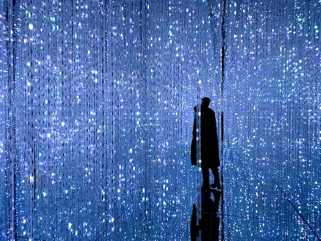 a person stands in a seemingly endless rooms of blue strands of twinkle lights