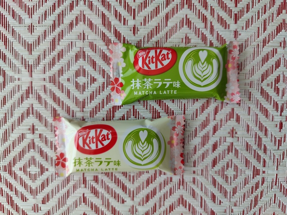 Two pieces of wrapped Matcha Latte KitKat from a Tokyo Treat subscription box. One wrapper is green and the other is white.