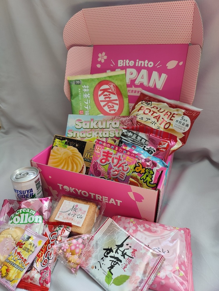 Tokyo Treat Japanese subscription snack box opened to show the following items: matcha latte KitKat, potato chips, a culture guide, kids' candy, pear tart, Japanese soda, sakura-flavored cookies, ramen, and sakura rice crackers